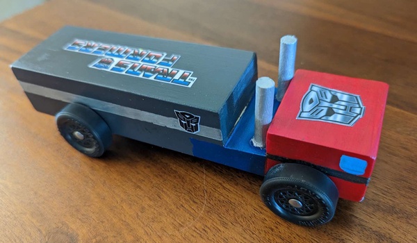 A pinewood derby car shaped and painted like the character Optimus Prime from Transformers, a semi-truck with a red cab and gray trailer.
